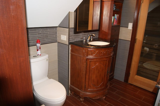 half bath featuring wood finish floors, vanity, toilet, and tile walls