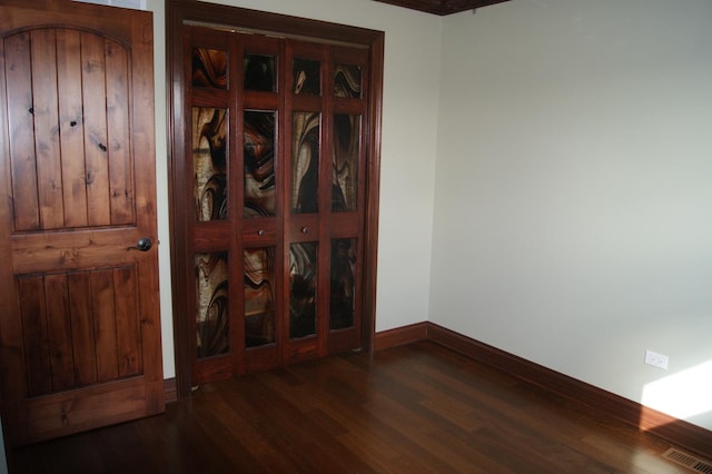 unfurnished room with dark wood-type flooring, visible vents, and baseboards