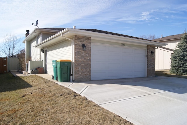 view of side of property featuring an attached garage, fence, concrete driveway, and brick siding