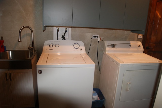 clothes washing area with washer and clothes dryer, a sink, cabinet space, and tile walls