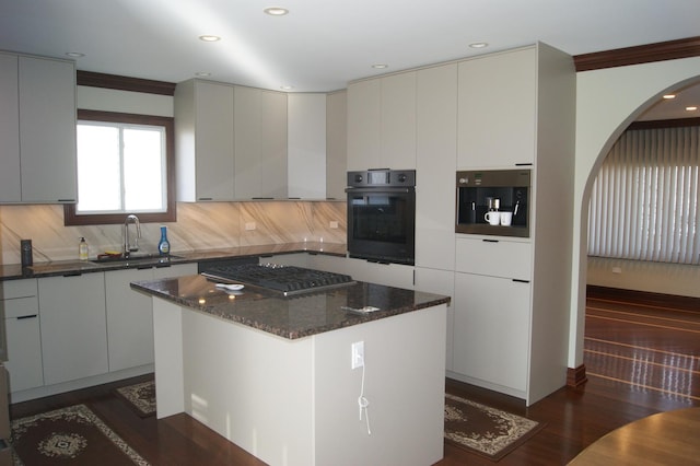 kitchen featuring tasteful backsplash, arched walkways, stainless steel gas cooktop, a sink, and black oven