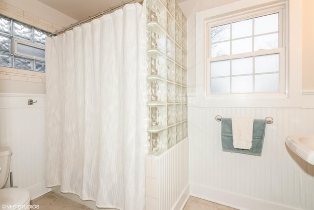 full bathroom featuring tile patterned flooring, wainscoting, curtained shower, and toilet