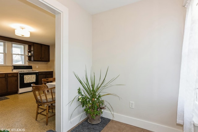 kitchen featuring range with gas stovetop, baseboards, open shelves, light countertops, and dark brown cabinets