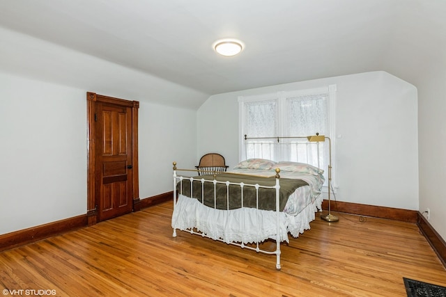 bedroom featuring baseboards, vaulted ceiling, and light wood finished floors