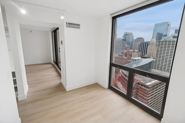 corridor featuring baseboards, visible vents, wood finished floors, rail lighting, and a city view