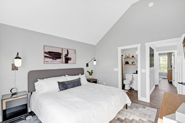 bedroom featuring lofted ceiling, ensuite bath, baseboards, and wood finished floors