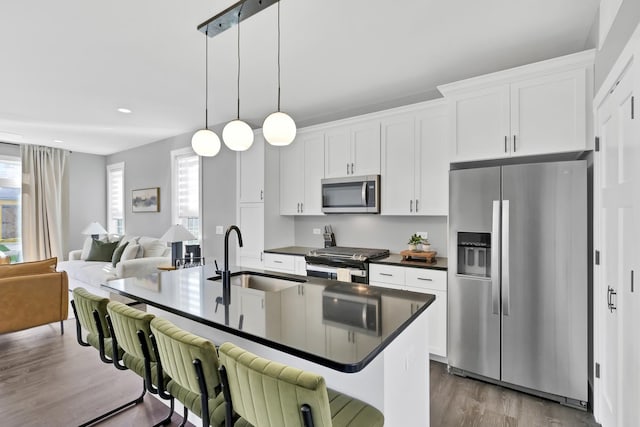 kitchen with a breakfast bar area, stainless steel appliances, dark countertops, white cabinetry, and a sink