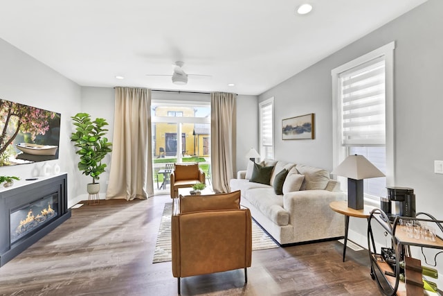 living room featuring baseboards, a ceiling fan, a glass covered fireplace, wood finished floors, and recessed lighting