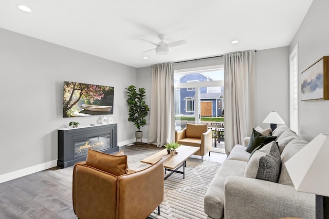 living room featuring ceiling fan, wood finished floors, a glass covered fireplace, and baseboards