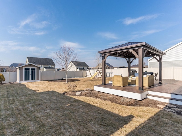 view of yard featuring an outbuilding, a deck, a playground, a fenced backyard, and a storage shed