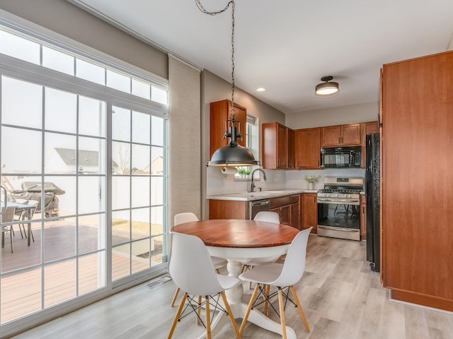 kitchen featuring brown cabinets, light countertops, light wood-type flooring, black appliances, and a sink