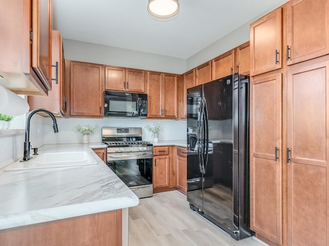 kitchen with light wood-style floors, brown cabinetry, a sink, light stone countertops, and black appliances