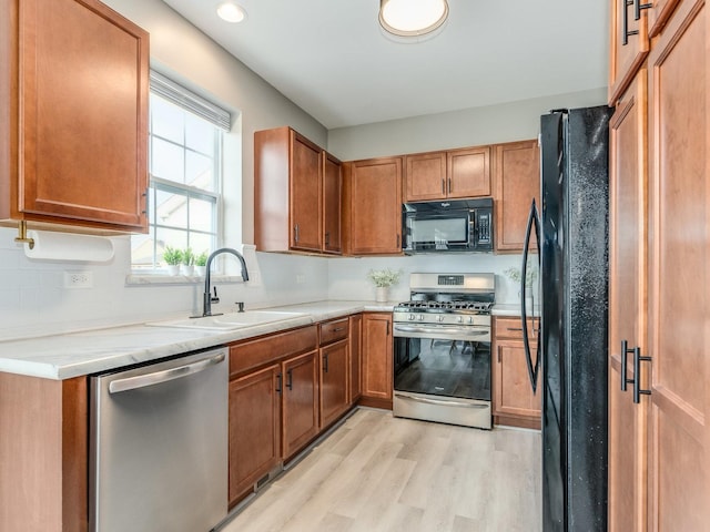 kitchen featuring brown cabinets, light countertops, light wood-style floors, a sink, and black appliances