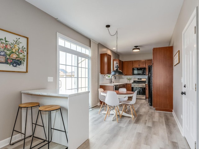 kitchen featuring light wood finished floors, a peninsula, stainless steel gas range, light countertops, and black microwave