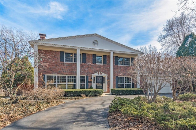 neoclassical home with aphalt driveway, an attached garage, brick siding, and a chimney