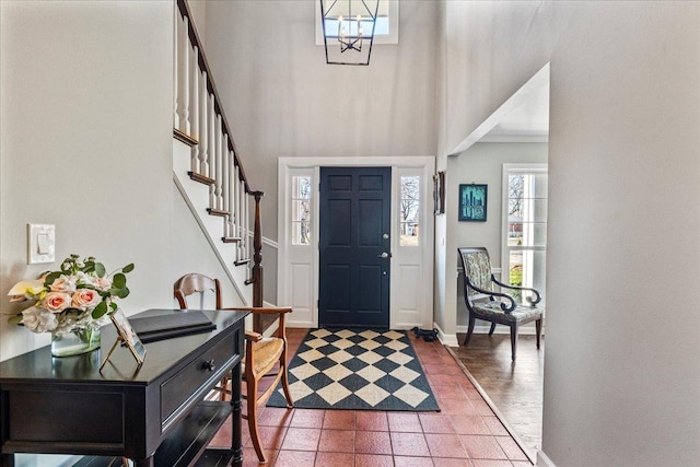 entryway with stairs, a high ceiling, a notable chandelier, and baseboards