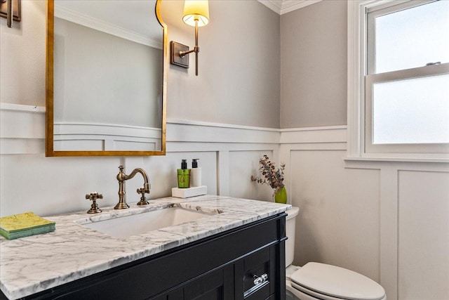 bathroom with a wainscoted wall, toilet, crown molding, a decorative wall, and vanity