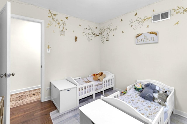 bedroom with a crib, wood finished floors, visible vents, and baseboards