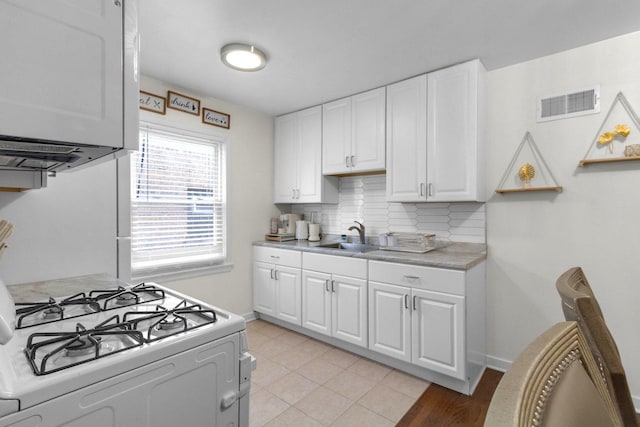 kitchen with white gas stove, light countertops, visible vents, backsplash, and a sink