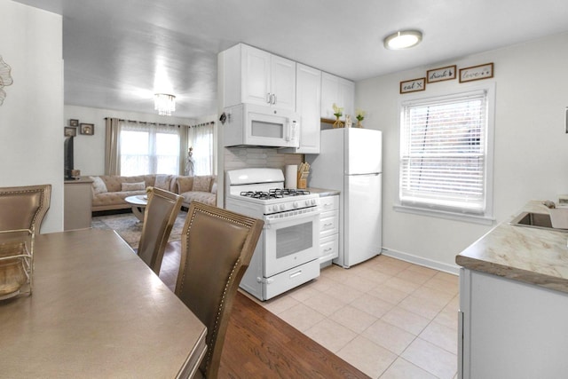 kitchen featuring light tile patterned floors, open floor plan, white cabinets, white appliances, and baseboards