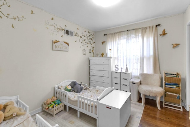 bedroom with a nursery area, visible vents, and wood finished floors
