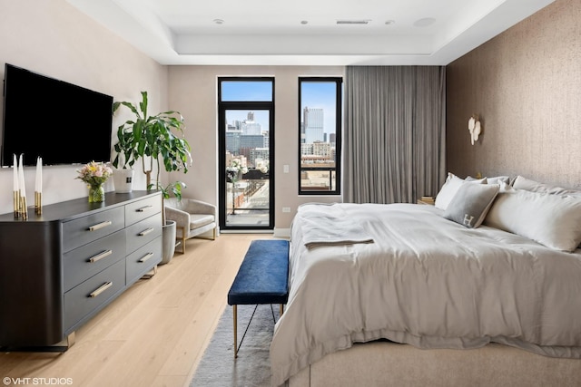 bedroom featuring visible vents, a city view, a tray ceiling, light wood-style floors, and access to outside