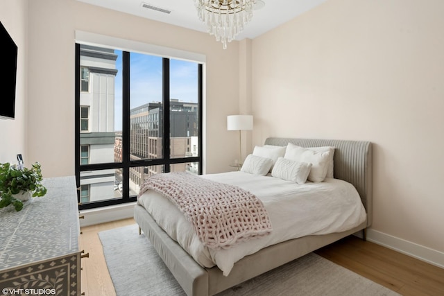 bedroom with visible vents, baseboards, an inviting chandelier, and wood finished floors