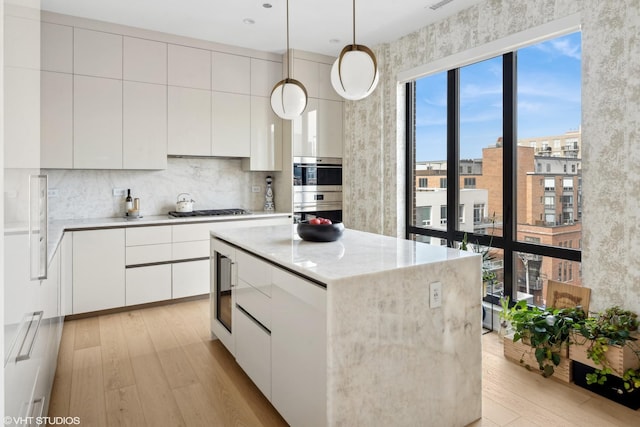 kitchen with light wood finished floors, a center island, gas stovetop, stainless steel double oven, and white cabinetry