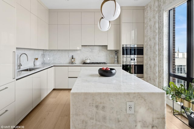 kitchen with modern cabinets, a sink, gas cooktop, stainless steel double oven, and decorative backsplash