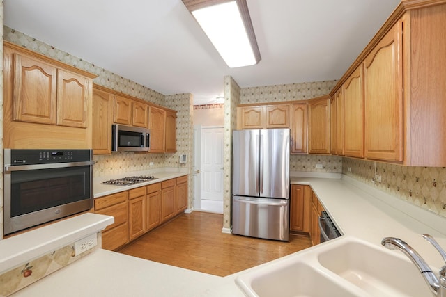 kitchen featuring a sink, light countertops, appliances with stainless steel finishes, light wood finished floors, and wallpapered walls