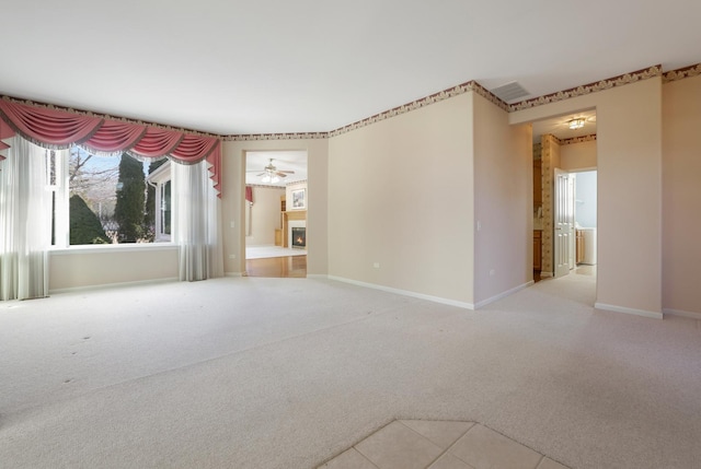 carpeted empty room featuring a warm lit fireplace, ceiling fan, visible vents, and baseboards