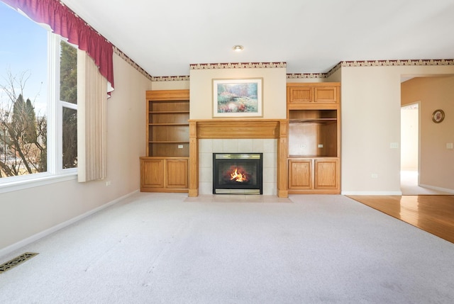 unfurnished living room with baseboards, a fireplace, visible vents, and light colored carpet