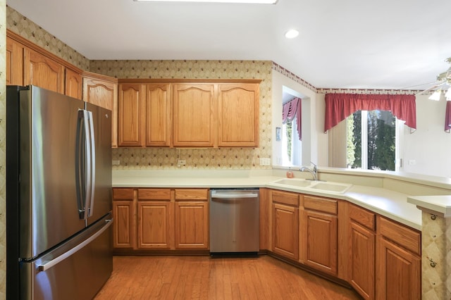 kitchen featuring light wood-style flooring, stainless steel appliances, a sink, light countertops, and wallpapered walls