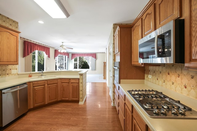 kitchen with stainless steel appliances, a peninsula, a sink, light wood-style floors, and light countertops