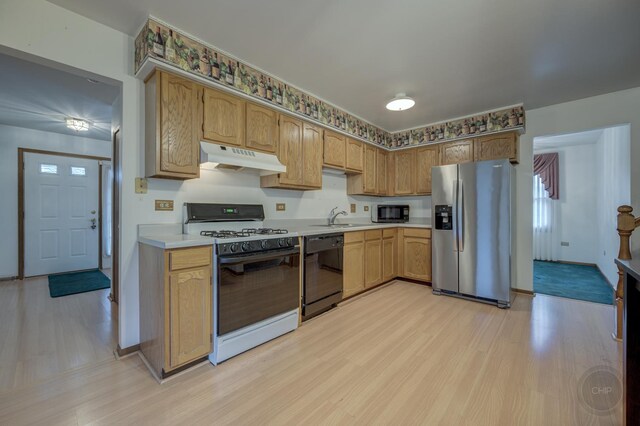 kitchen with light countertops, a sink, light wood-type flooring, under cabinet range hood, and black appliances