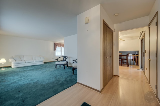 corridor with light wood finished floors, baseboards, and light colored carpet