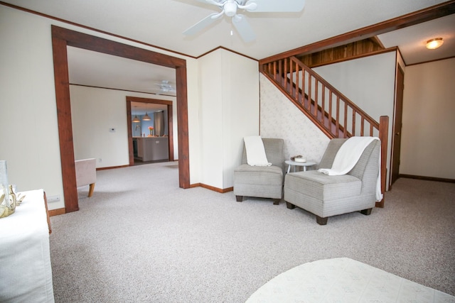 sitting room with carpet flooring, a ceiling fan, baseboards, stairs, and crown molding