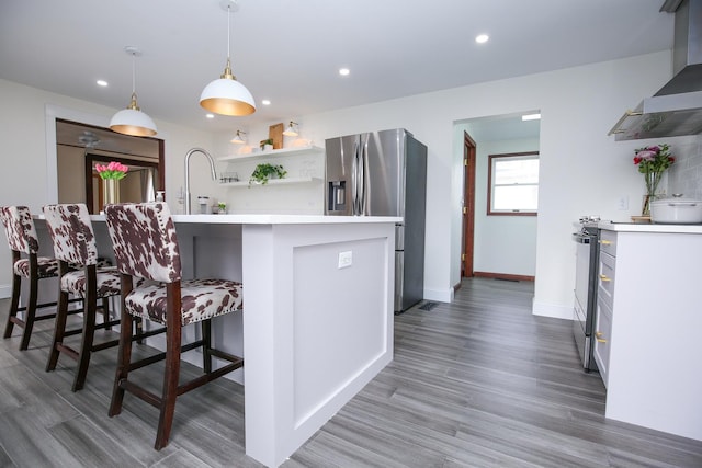 kitchen with wall chimney exhaust hood, appliances with stainless steel finishes, a breakfast bar, light countertops, and open shelves