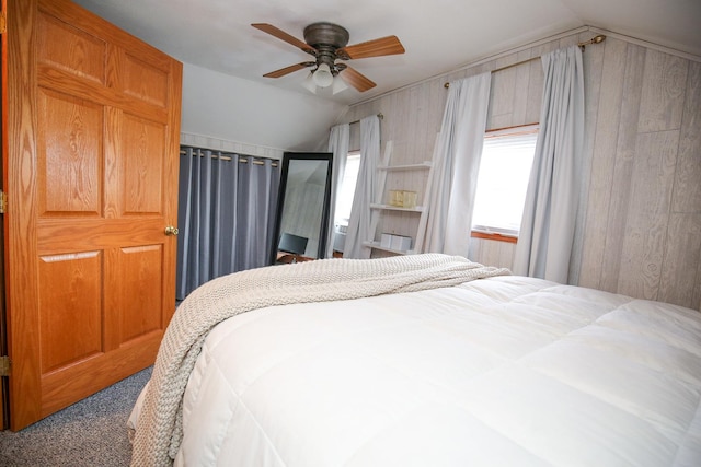 bedroom featuring vaulted ceiling, wood walls, carpet, and a ceiling fan