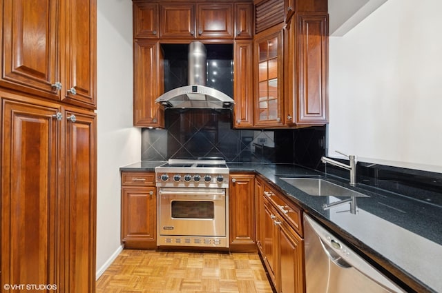 kitchen with brown cabinets, stainless steel appliances, tasteful backsplash, a sink, and wall chimney range hood