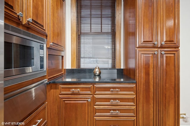 kitchen with brown cabinets, dark stone counters, stainless steel microwave, and a warming drawer