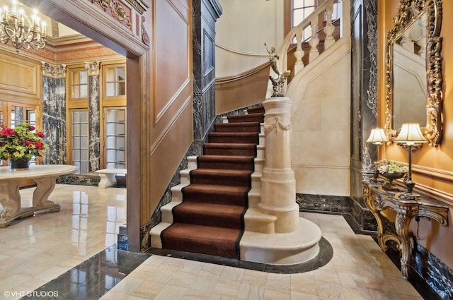 interior space with stairway, ornamental molding, marble finish floor, an inviting chandelier, and a decorative wall