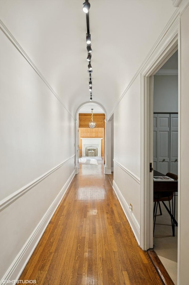 corridor featuring arched walkways, hardwood / wood-style floors, ornamental molding, and baseboards