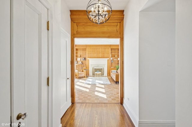 corridor with baseboards, wood finished floors, built in features, and an inviting chandelier