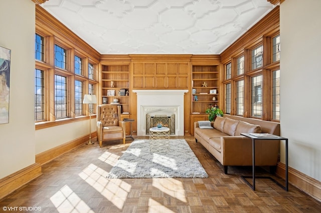 sitting room with a lit fireplace, built in shelves, baseboards, and ornamental molding