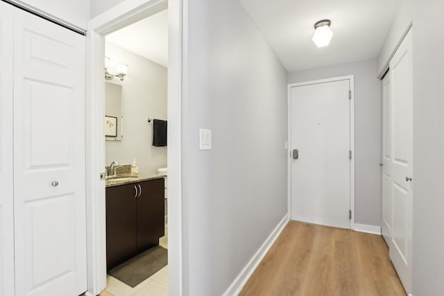 hallway with light wood-style floors, baseboards, and a sink