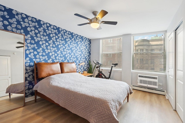 bedroom featuring wallpapered walls, baseboards, a baseboard radiator, an accent wall, and wood finished floors