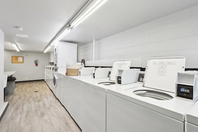 common laundry area featuring baseboards, stacked washer and dryer, light wood-type flooring, and washer and dryer