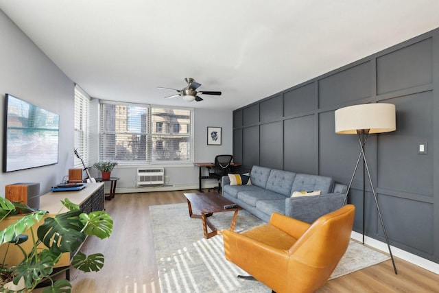 living room with a wall unit AC, a decorative wall, light wood-style flooring, and ceiling fan