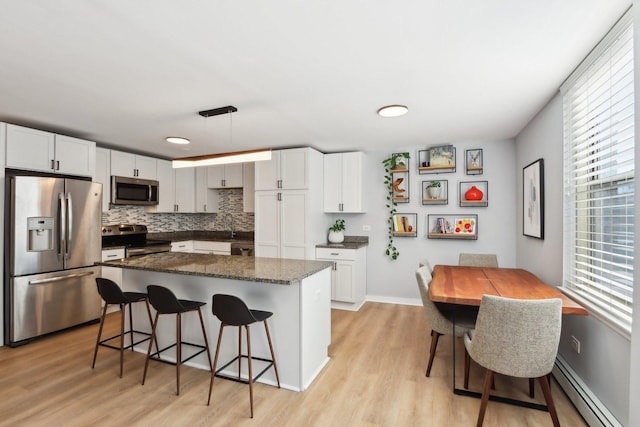 kitchen featuring a baseboard heating unit, stainless steel appliances, white cabinets, and a kitchen breakfast bar